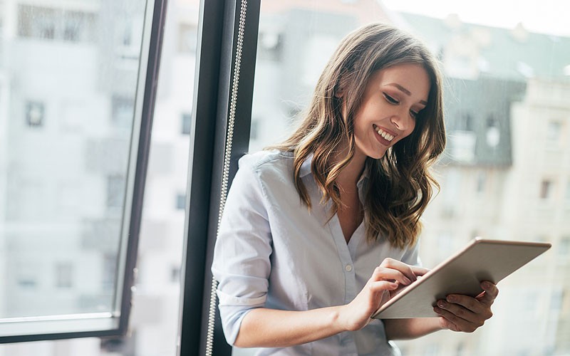 smiling-businesswoman-holding-tablet-in-front-of-window smiling-businesswoman-holding-tablet-in-front-of-window