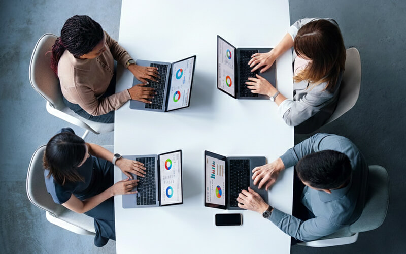 Modern Office Team Collaboration Top-down view of diverse professionals collaborating around laptops and documents in a modern open office workspace.
