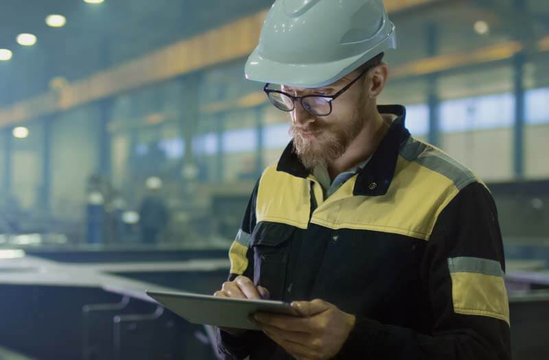Engineer reviewing technical plans on a tablet computer while seated at a worktable in a modern workspace. Engineer Using Tablet at Workspace