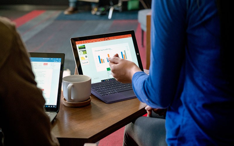 Two people collaborating in a library on Surface devices.