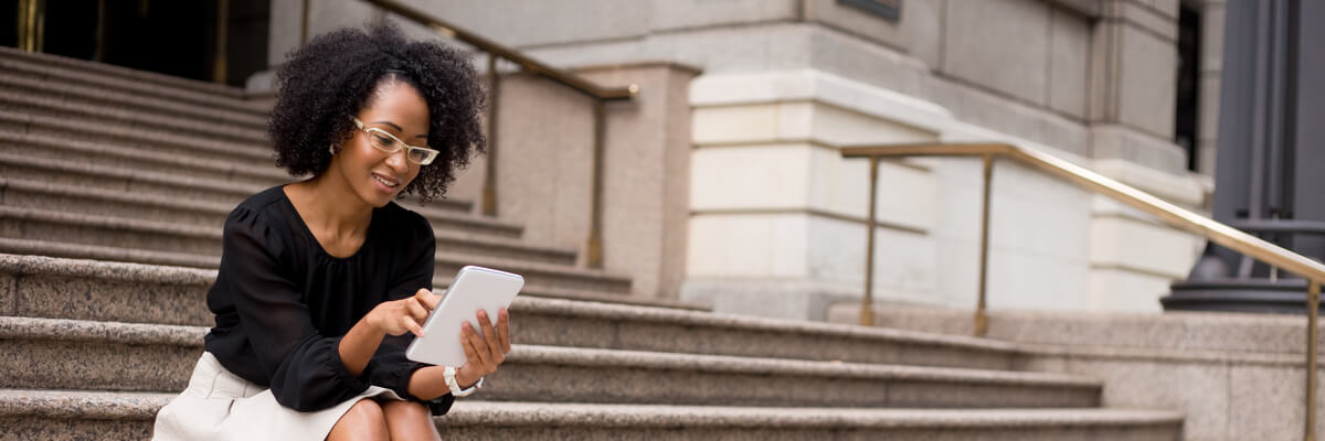 Managing device risk in government BYOD programs Business woman checking email on her personal tablet computer sitting on the steps of a government building