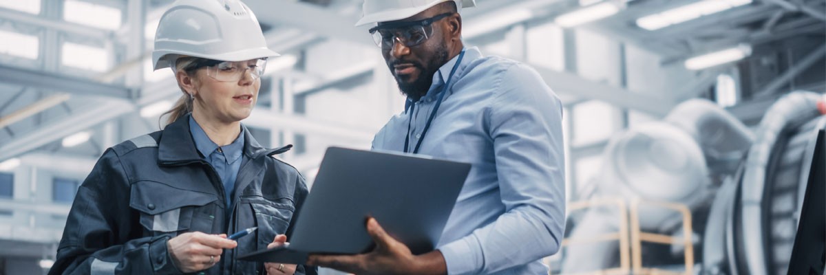 Explore the latest innovations connecting the factory floor. Two engineers on factory floor looking at laptop computer