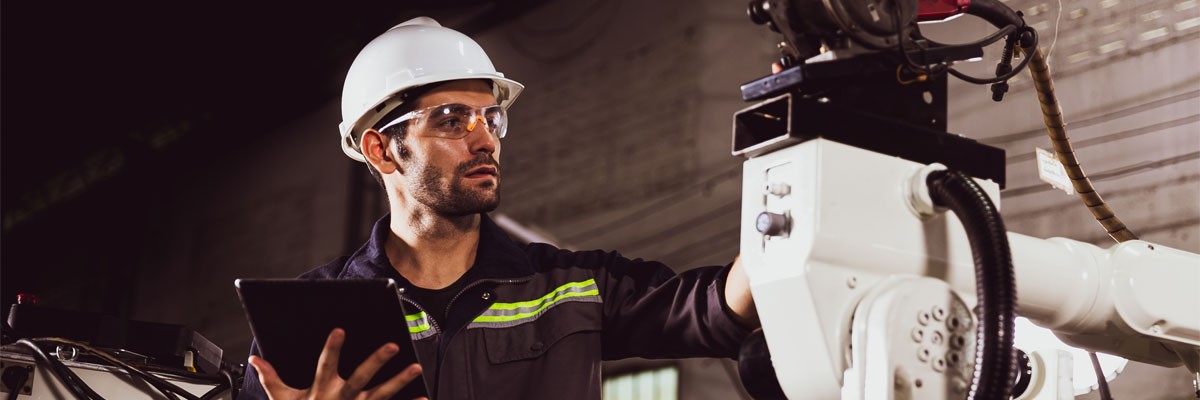 Harnessing data analytics can improve crucial areas of your connected factory Man in hard hat works with manufacturing robotics technology with tablet device