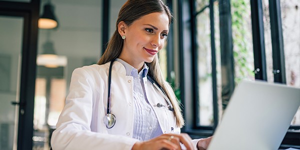 Discover how cloud-based Barco healthcare solutions empower clinical staff to deliver better patient care. Nurse working on laptop computer. Reading report.