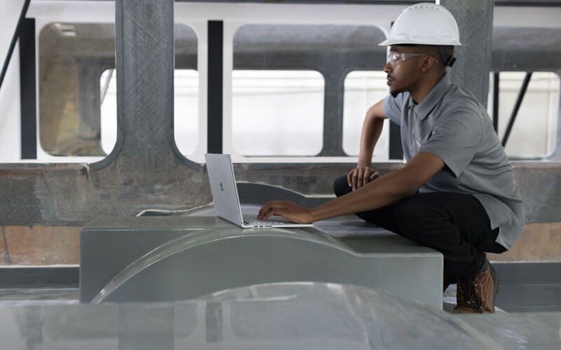 Discover how Microsoft Surface devices offer benefits to the manufacturing industry Man in hard hat works in manufacturing industry with Surface device