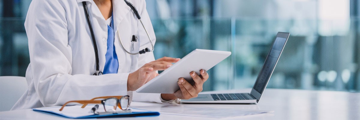 Healthcare Company Scales and Modernizes IT to Address Rapid Growth Demands Doctor holding tablet device with patient data while sitting at desk with laptop computer