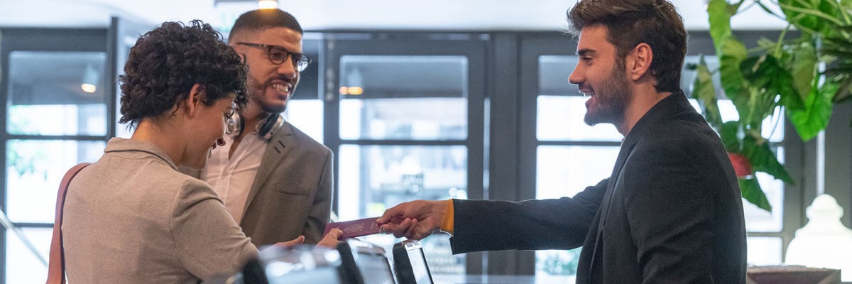 A global hotel chain leverages professional device services for fast resolution and service delivery, streamlined user and customer experiences, and little to no downtime. Hotel guests checking into a hotel. Supply chain optimization, device services, device management, provisioning, break-fix, refresh, support, customized procurement catalog