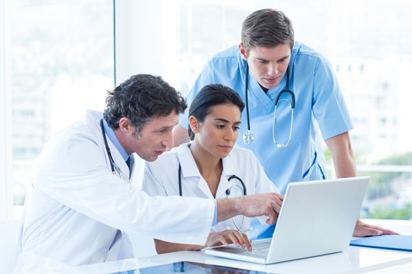 Growing mobile and IoT technology presents a number of security and management challenges. Three doctors in an office conferring at a desktop.
