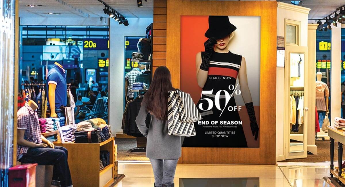 How to take advantage of the change in visual displays and capitalize on consumer interaction Woman holding shopping bags faces a promotional sale banner outside of a retail window
