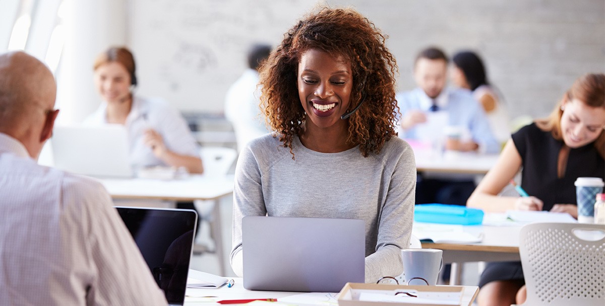 Your contact center is critical to running your business efficiently and keeping customers happy, making it imperative to keep it up to date. Female worker at contact center appears to be smiling while typing on computer laptop