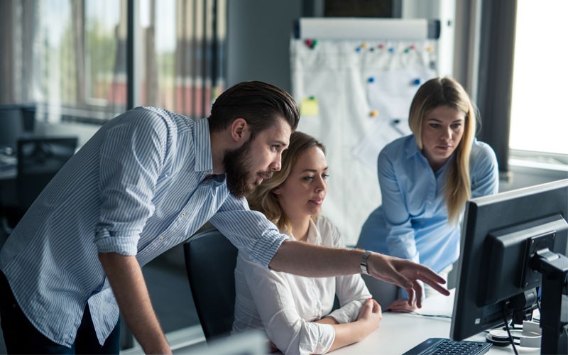 Reduce your costs and improve your operations. Team working off desktop computers in open concept office