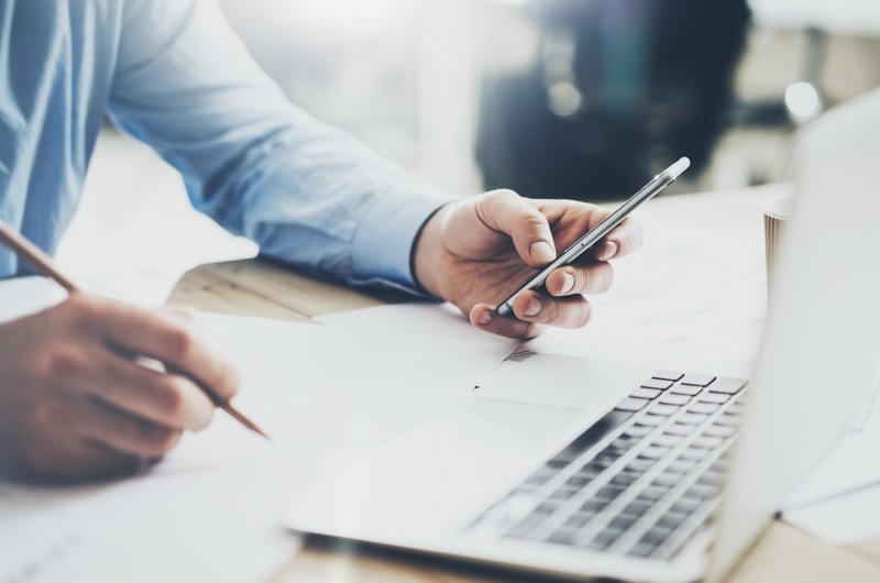 Unify mobile and desktop operations Business man looking at phone while using laptop.