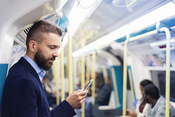 Subway passenger looking at phone Businessman reading article on iPhone while on the subway