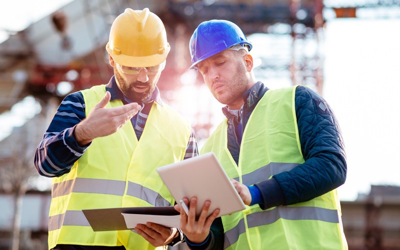 Technology is constantly improving the way we construct things Two engineers at construction site looking at plans with tablet device