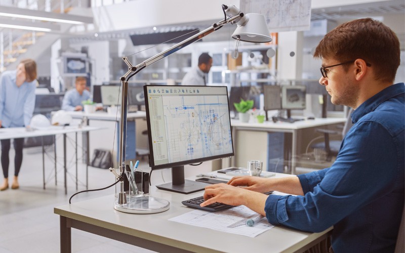 Create workflow efficiencies that free teams Businessman using CAD software on computer in open office